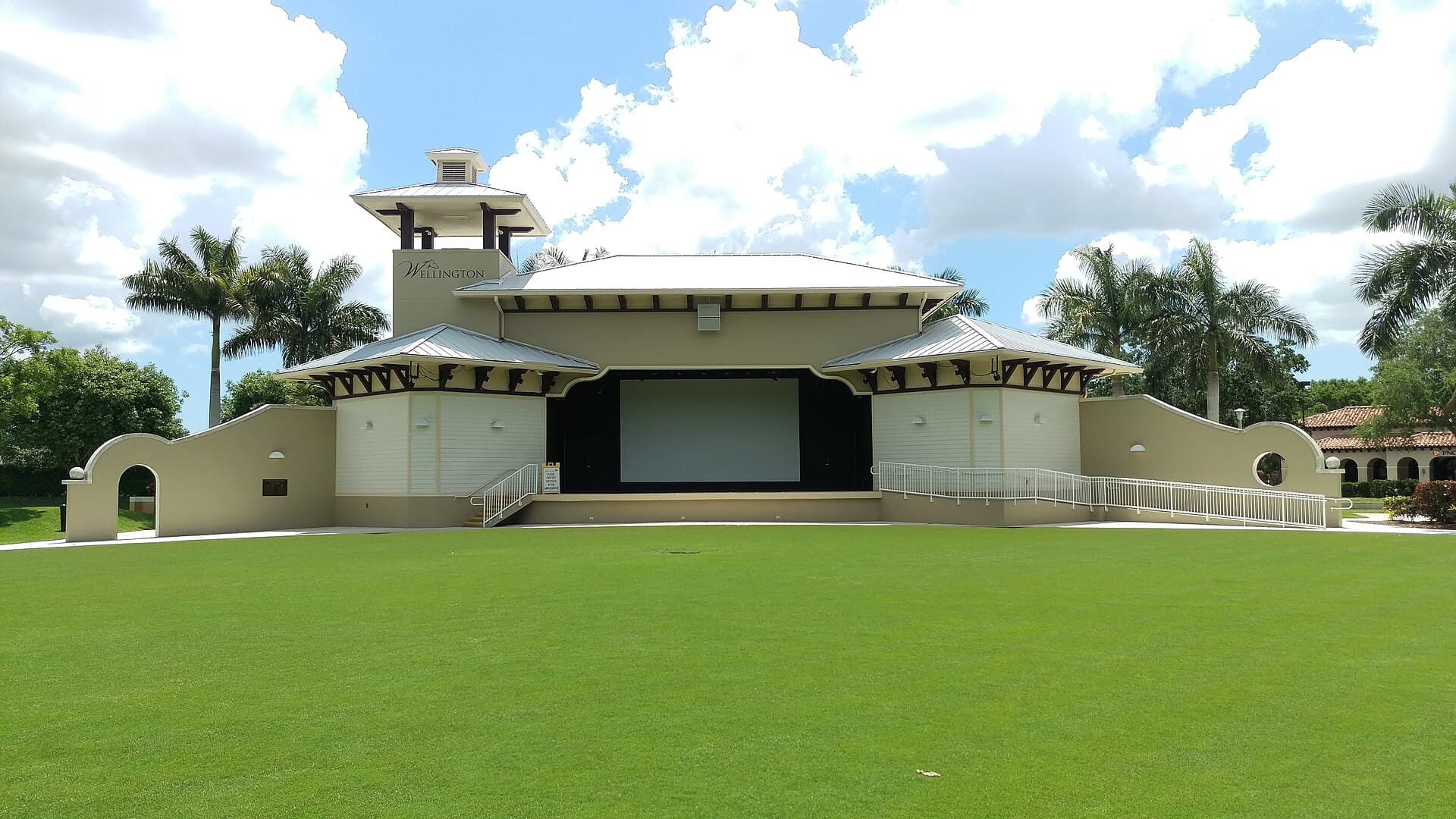 The Wellington Amphitheater stage and its open lawn under a blue sky with palm trees, Wellington, Florida