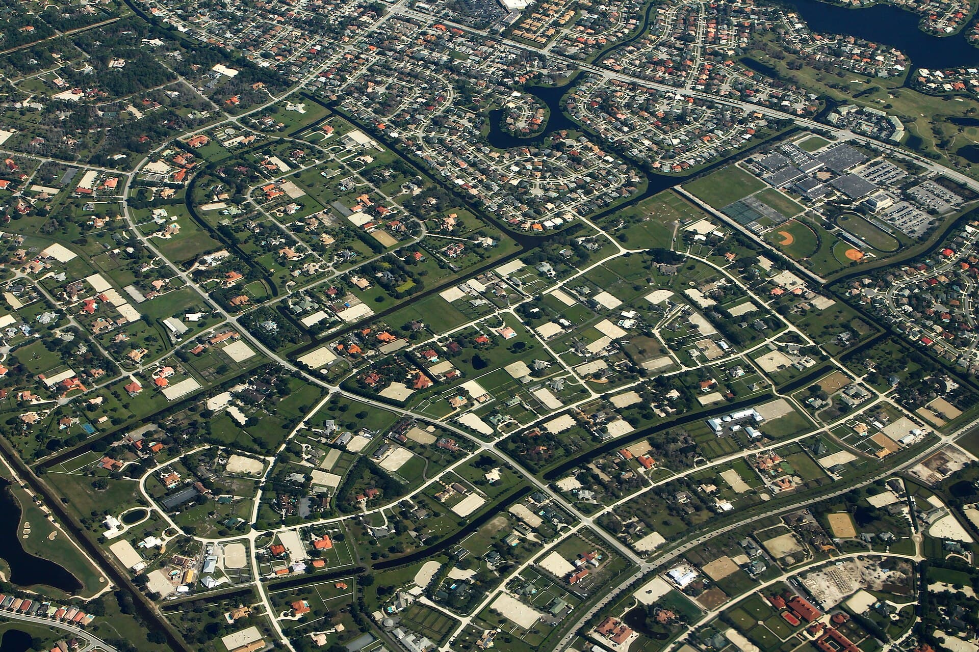 Aerial view of Wellington, Florida: acreage lots with riding arenas beside planned neighborhoods and a lake